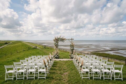 Strandhochzeit an der Wurster Nordseeküste: Zeremonie-Aufbau mit weißen Stühlen auf dem Deich am Wattenmeer